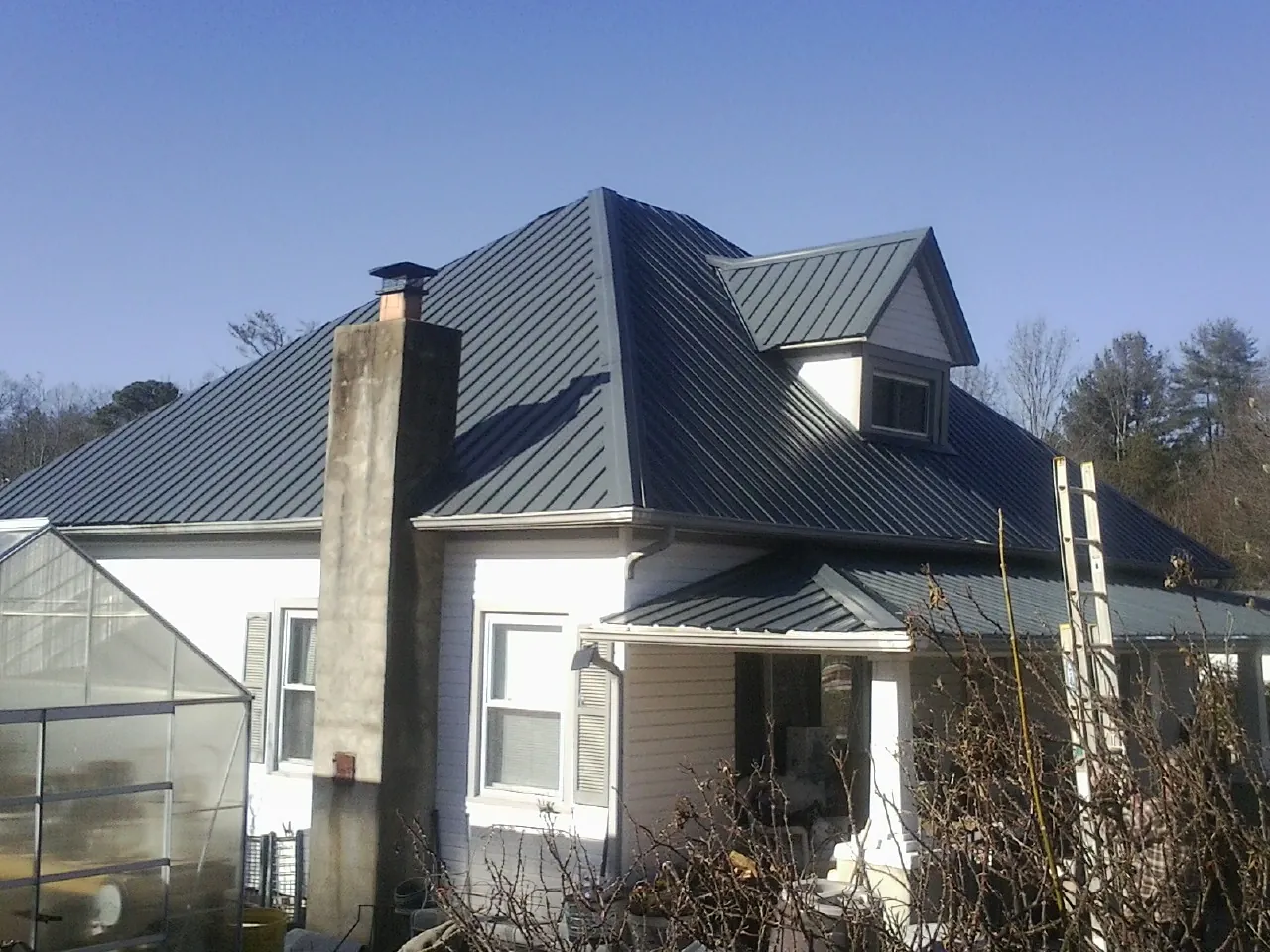 Dark blue standing seam metal roof on a white farmhouse with dormer — Slate & Tile Roof Repair by Roofing Brothers in Spencerville