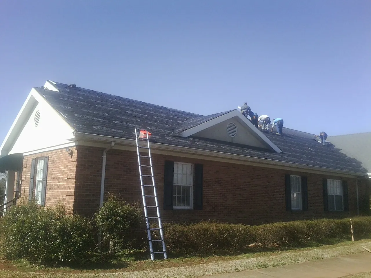 Crew tearing shingles off a brick ranch roof with a ladder set — Emergency Roof Repair work by our crew in Spencerville