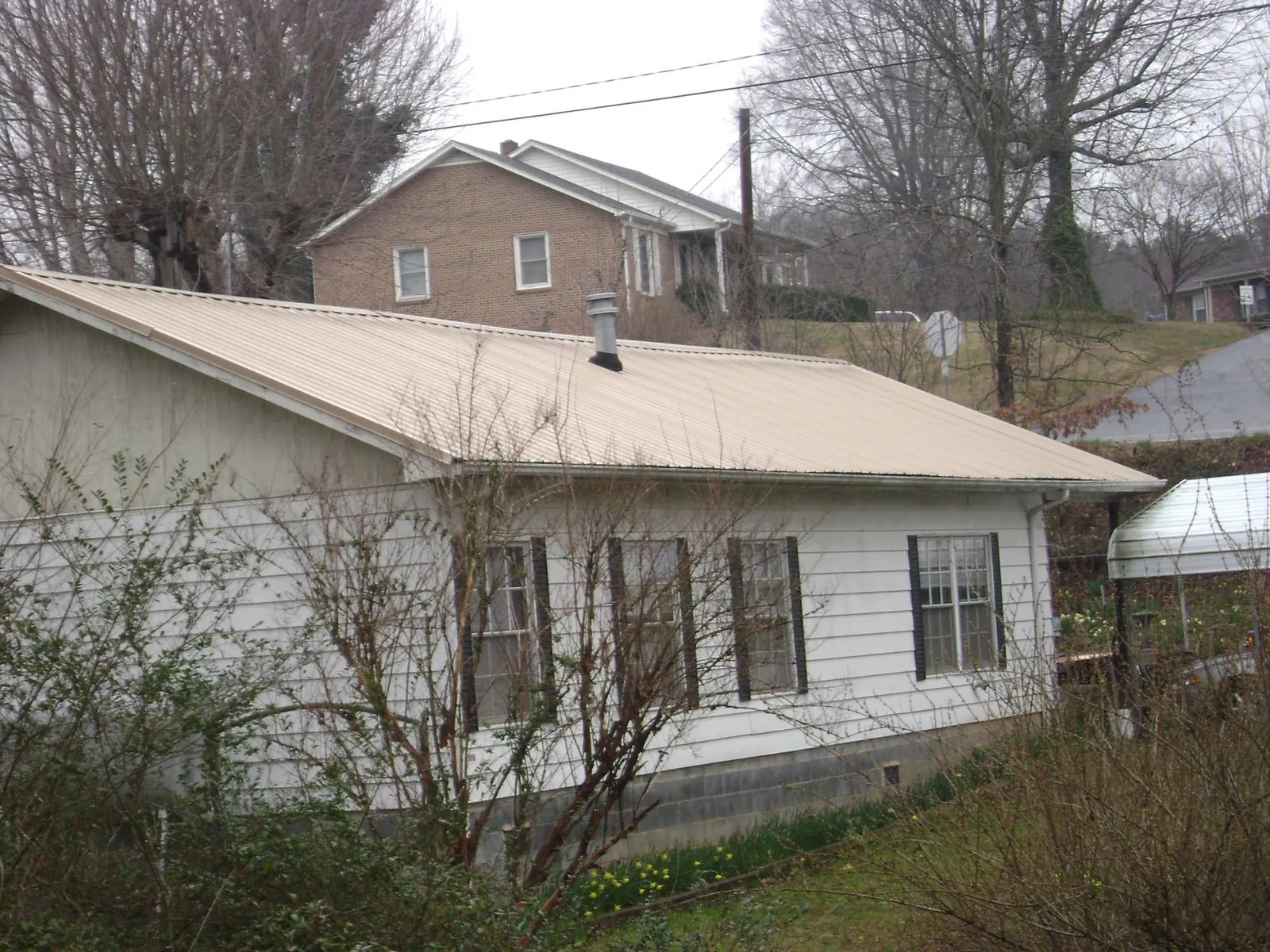 Tan metal roof on a white sided house set into a hillside — Commercial Roofing by Roofing Brothers in Spencerville