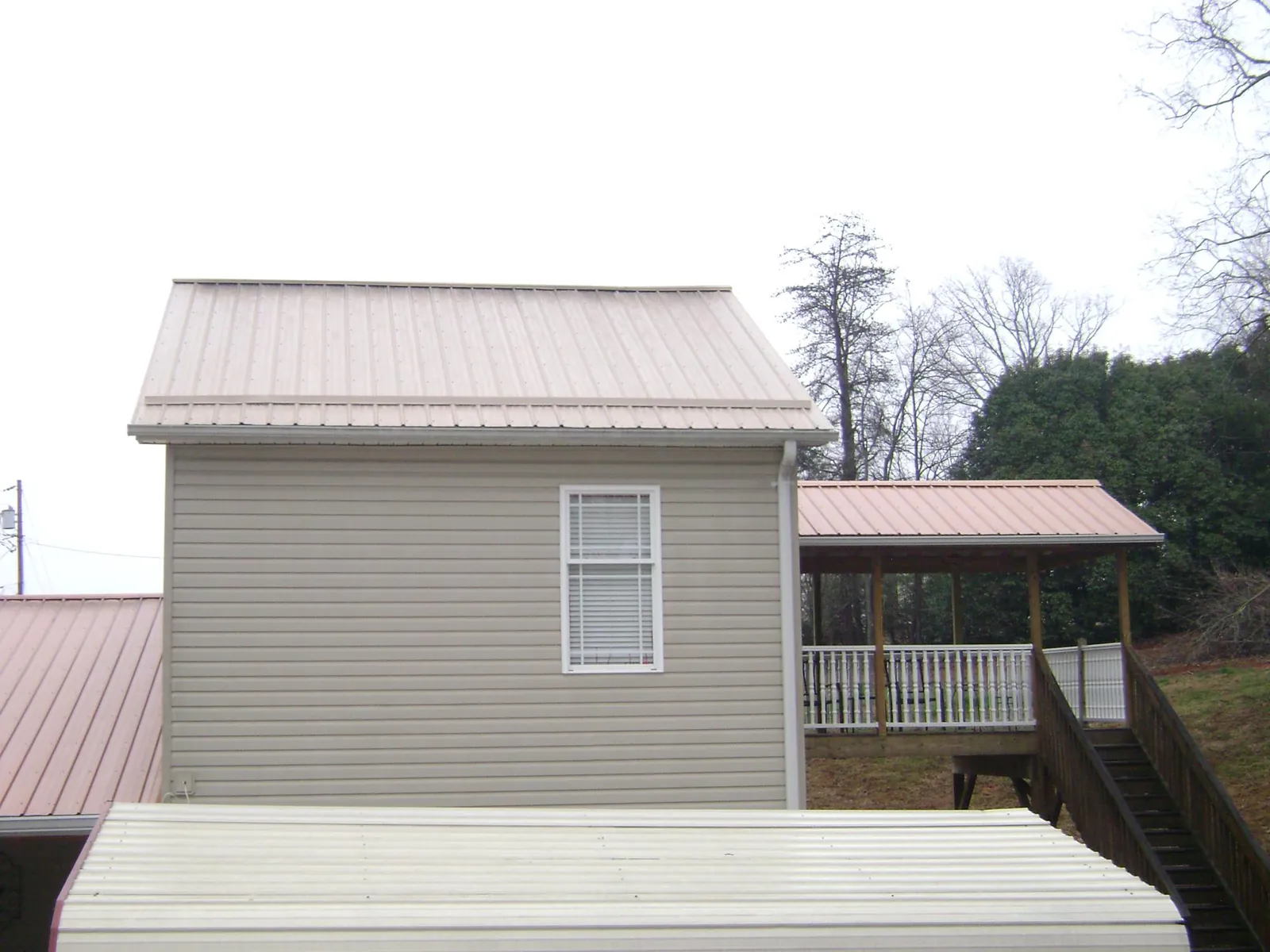 Tan metal roofs on a two story addition and attached porch, from a Roof Replacement job in Spencerville
